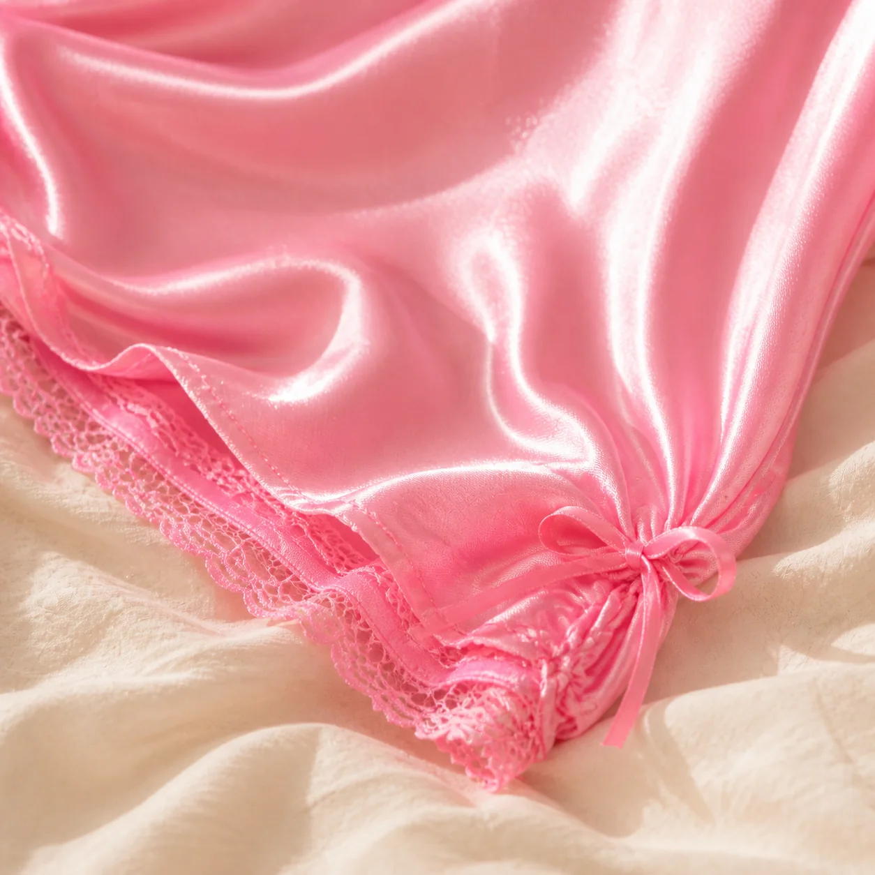 Close-up of the bright pink satin hem, lace edging and side tie